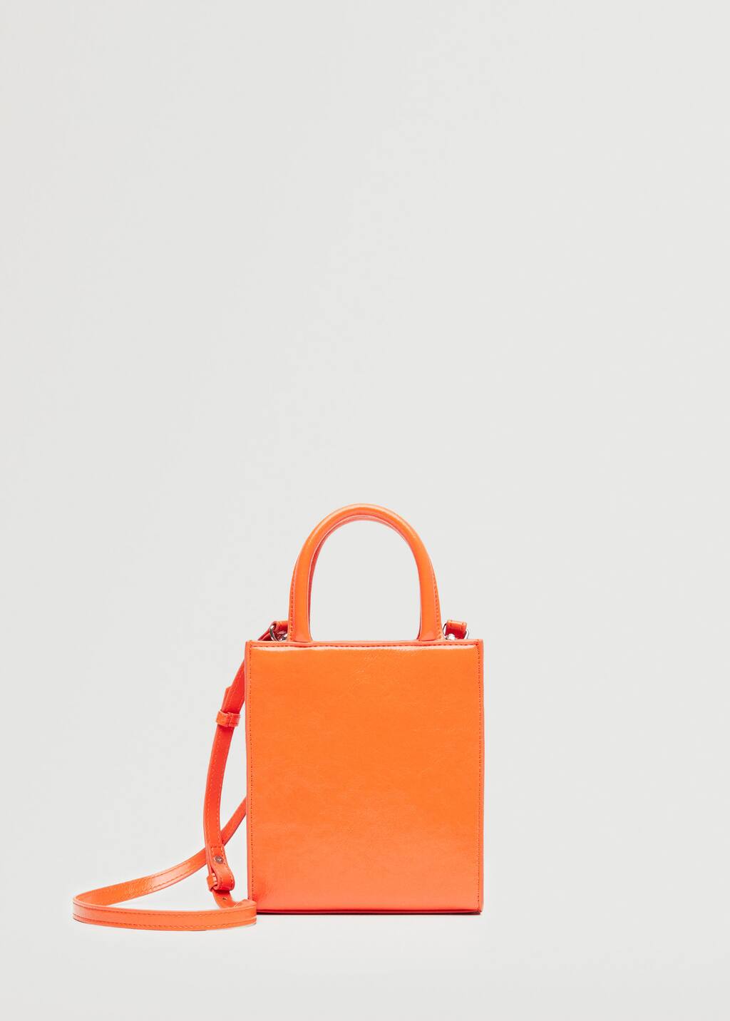 Mango Mini shopper bag. an orange bag is sitting against a white wall. 