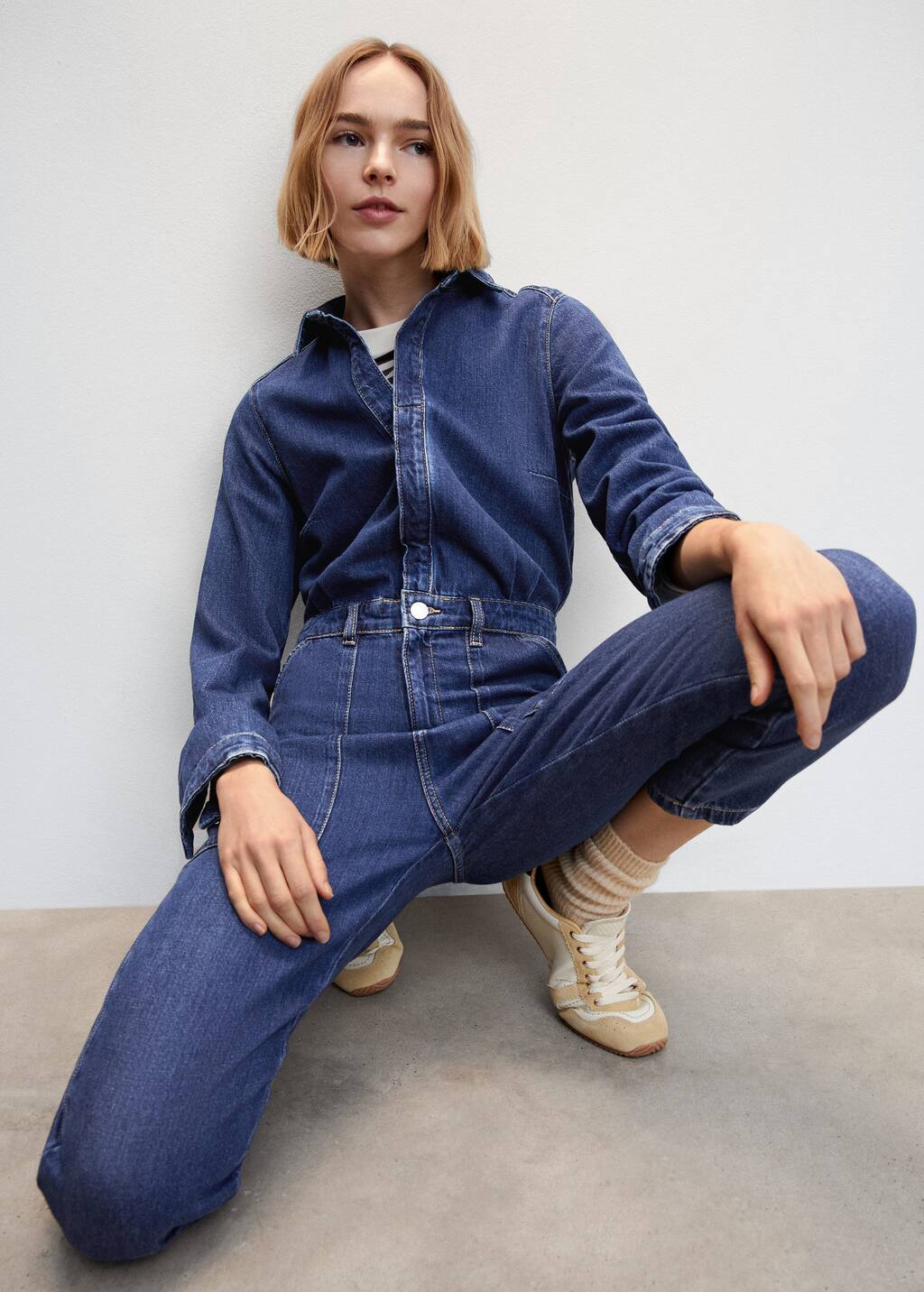 Mango Long denim jumpsuit. a woman squatting on the ground wearing a denim outfit. 