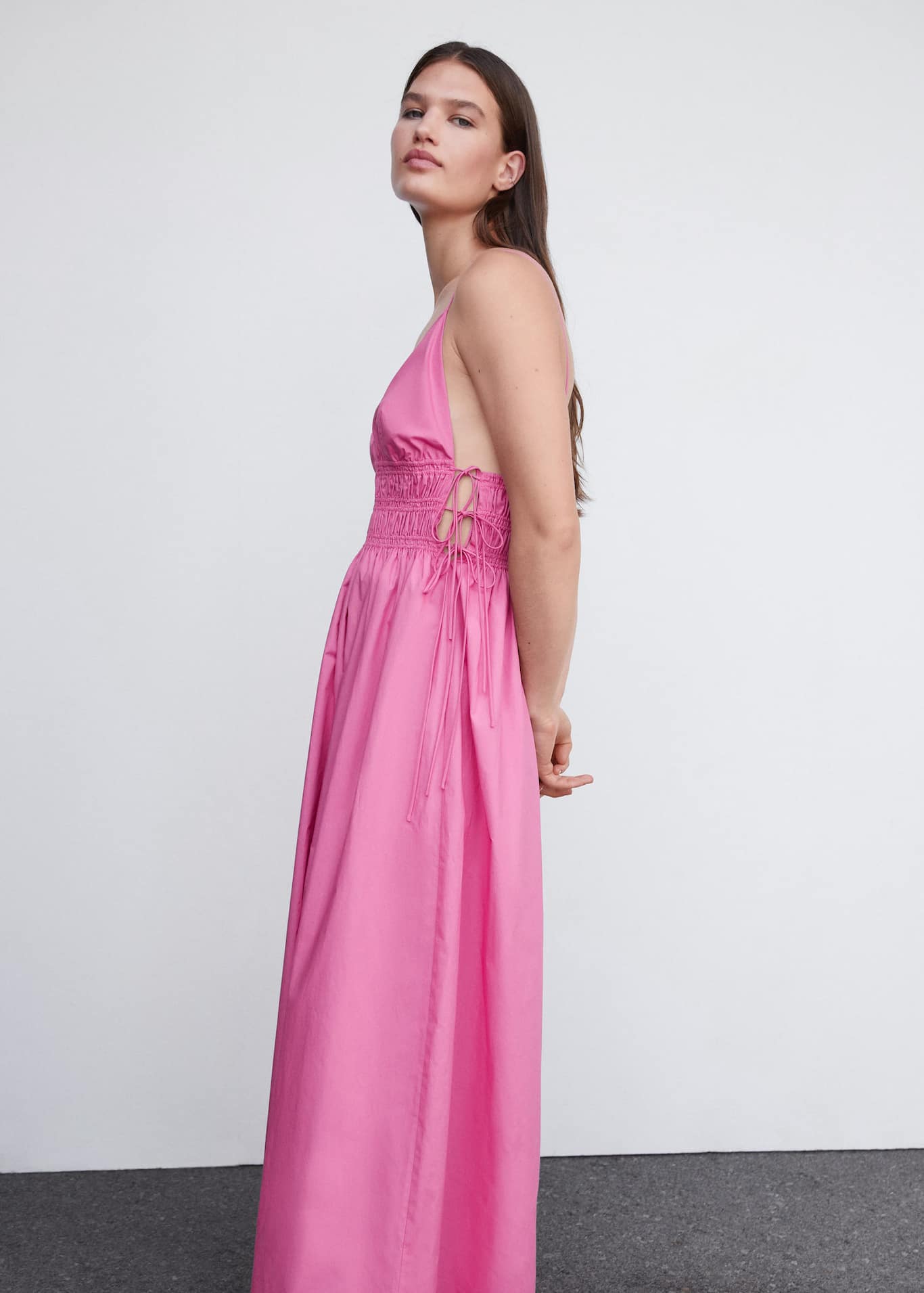 Spice up your summer party looks with Mango's pink maxi dress with side ties in 100% cotton fabric. It has a V-neck, thin straps and smocking under the bust which ties at the sides.